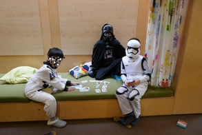Drei Kinder in Star Wars-Faschingskostümen sitzen in einer Spielnische bei einem Kartenspiel.