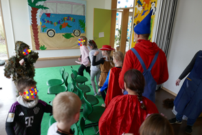Kinder tanzen maskiert im Kreis in einem Raum.