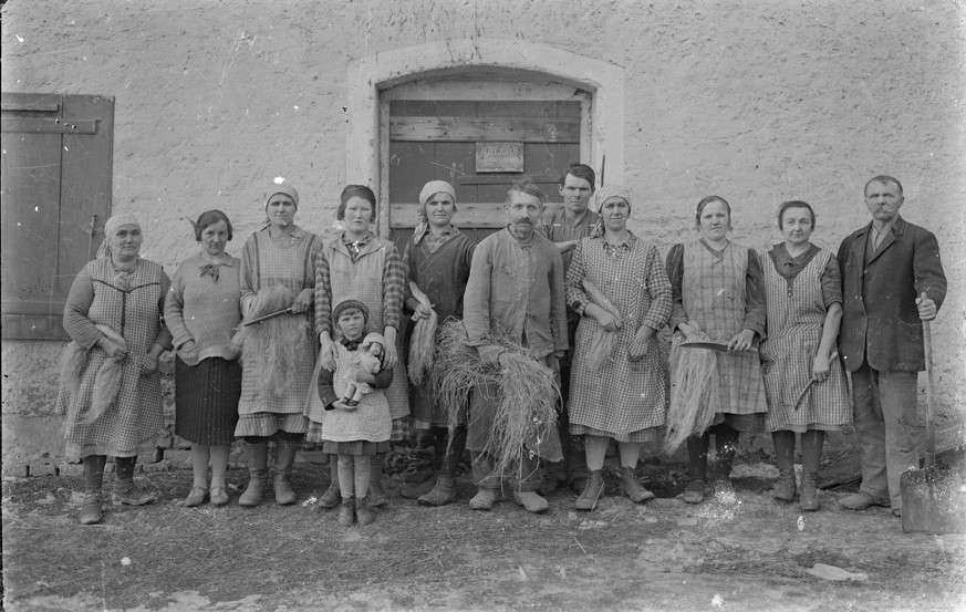 Bewohner im Braunauer Ländchen vor dem Brechhaus. Schwarzweiß-Aufnahme von Personen in ländlicher Umgebung vor einem Haus.