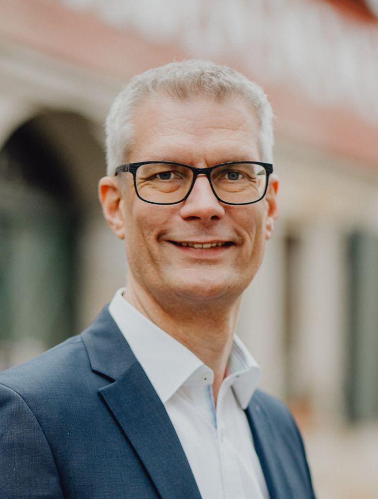 Oberbürgermeister Dr. Uwe Kirschstein im Stadtgespräch. Portrait des Oberbürgermeisters Dr. Uwe Kirschstein. Im Hintergrund sieht man schemenhaft die Fachwerkfassade mit Sandstein.