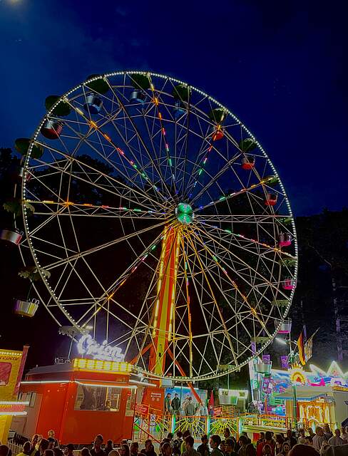 Ein beleuchtetes Riesenrad auf einem Festgelände bei Nacht.