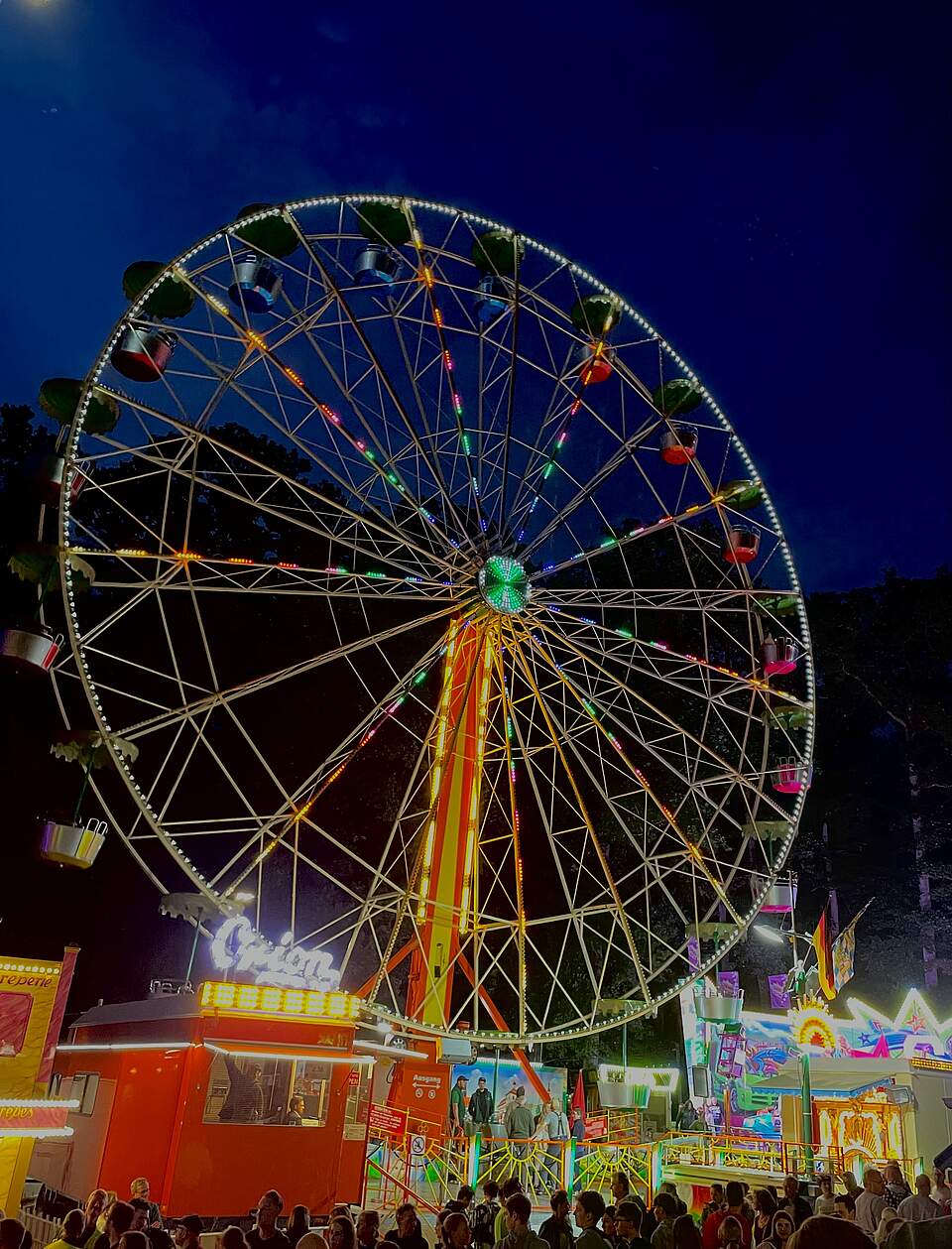 Ein beleuchtetes Riesenrad auf einem Festgelände bei Nacht.