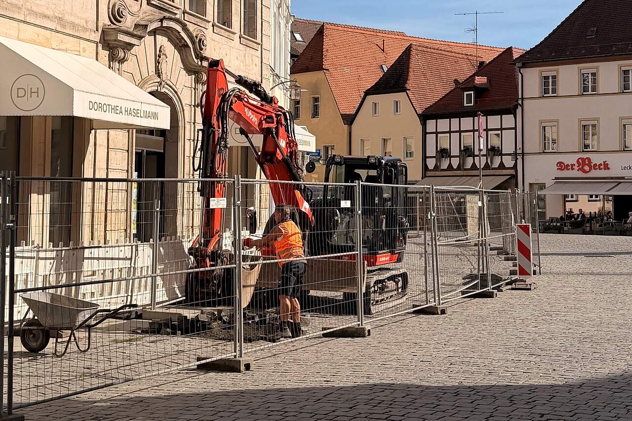 1. Bauabschnitt des Lichtkonzepts für den Rathausplatz in der Sattlertorstrasse. Bauarbeiten mit Entpflasterung durch einen Bagger am Rathausplatz vor einer Häuserzeile am Rathausplatz.