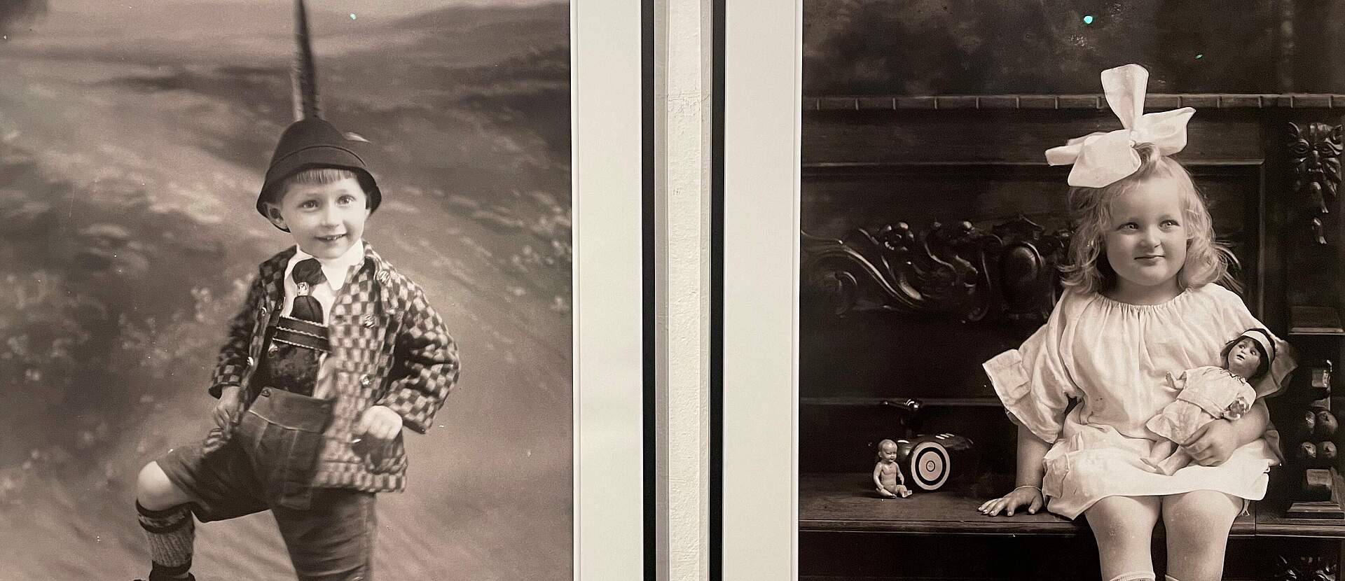 Zwei Fotografien aus den 1920er Jahren zeigen links einen kleinen Jungen in Tracht und Hut sowie recht ein Mädchen in einem weißen Kleid und einer großen Schleife im Haar.