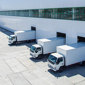 Drei LKWs parken an einem Logistikzentrum zum Ent- oder Beladen.