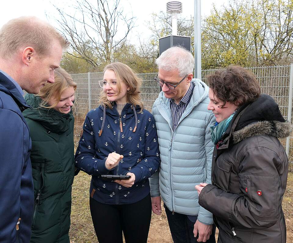 Personen um ein Tablet bei der Einweihung der Wetterstationen