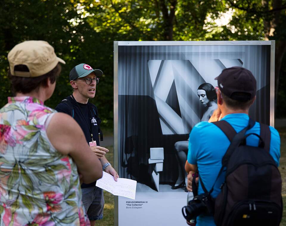 Besucher im Fotopark mit einem Führer vor einer Fotogtrafie 