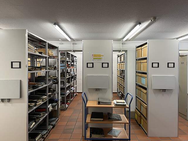 Ein Archivraum mit gefüllten Regalen und Transportwagen.