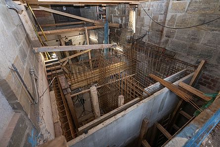 Blick von oben auf eine Baustelle im Keller eines großen historischen Gebäudes mit Holzstützen und Baustahlmatten.