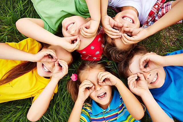 Kinder die im Gras liegen und nach oben gucken.