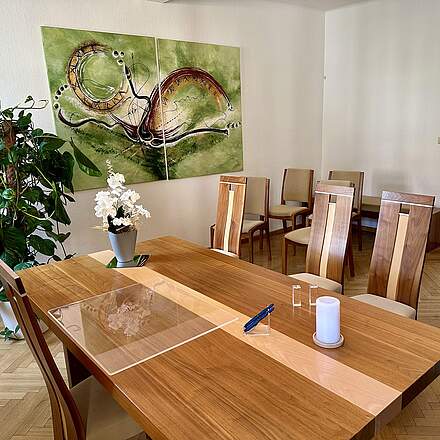Trauunngszimmer in Forchheim mit stilvollen Holzmöbeln, Zimmerpflanzen, einem großen Wandbild in Grüntönen. Auf dem Tisch des Standesbeamten stehet eine weiße Orchidee, eine weiße Kerze und zwei blaue Füller.