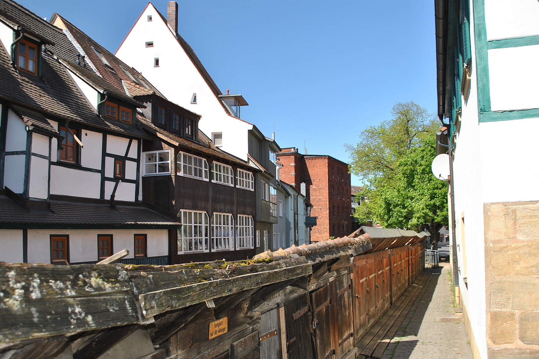 Historische Fischkästen auf Holz entlang der Wiesent. Im Hintergrund eine Häuserzeile der Altstadtbauten, teils mit Fachwerk und Holzverkleidung.