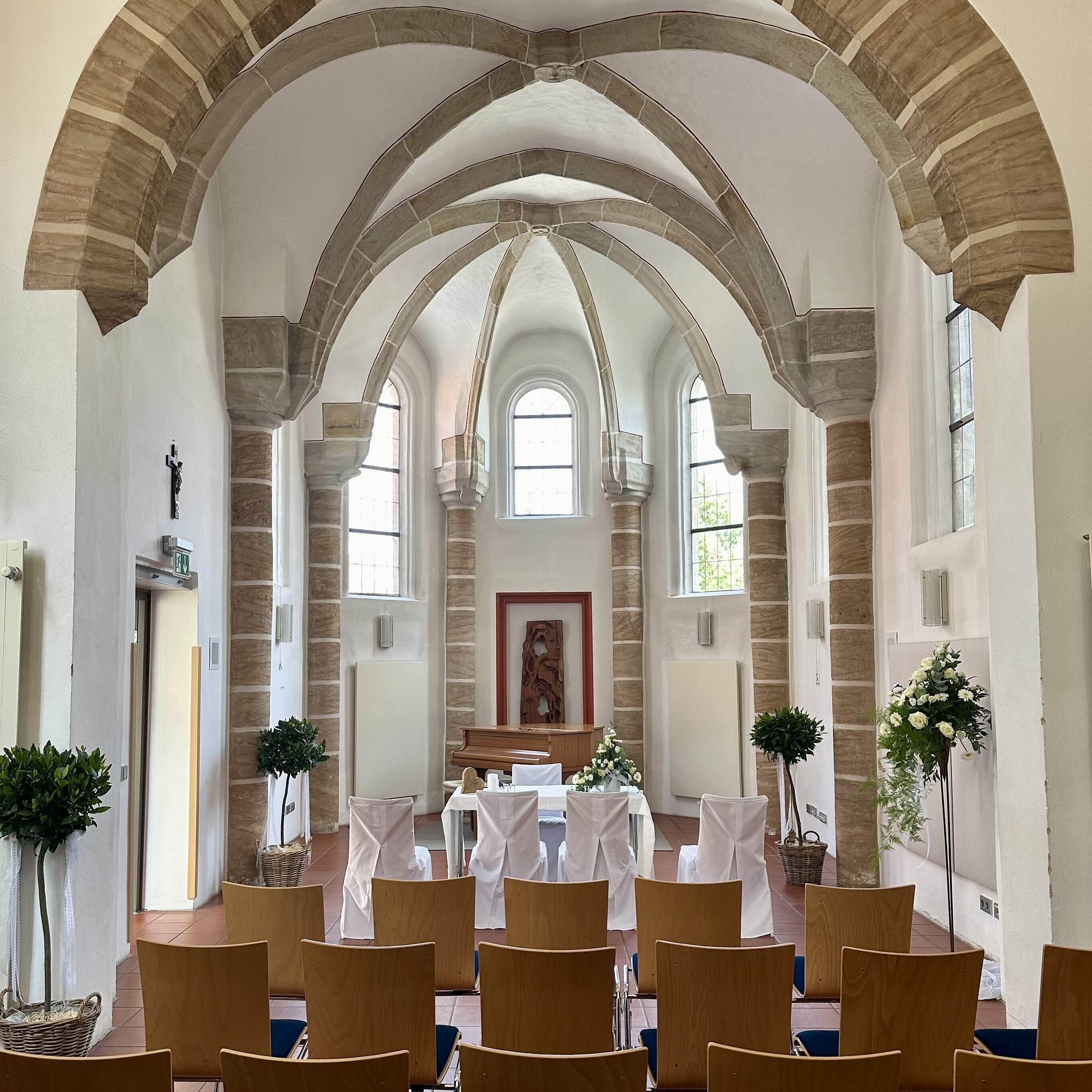 Der Innenraum der Kapelle St. Gereon mit Kreuzbogengewölbe, Stuhlreihen, Blumenschmuck und den weiß geschmückten Tisch des Standesbeamten von der Empore fotografiert.