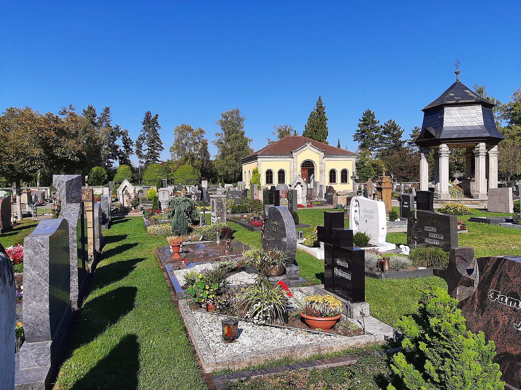 Kolumbarium und Dechant-Reuder-Kapelle im Alten Friedhof im Hintergrund. Im Vordfergrund befinden sich Erdgräber mit Bepflanzung.