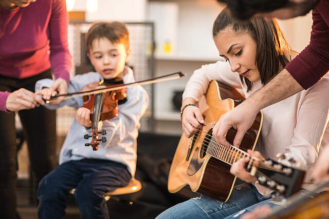 Kinder spielen Instrumente. Ein Junge spielt Geige und ein Mädchen spielt Gitarre.