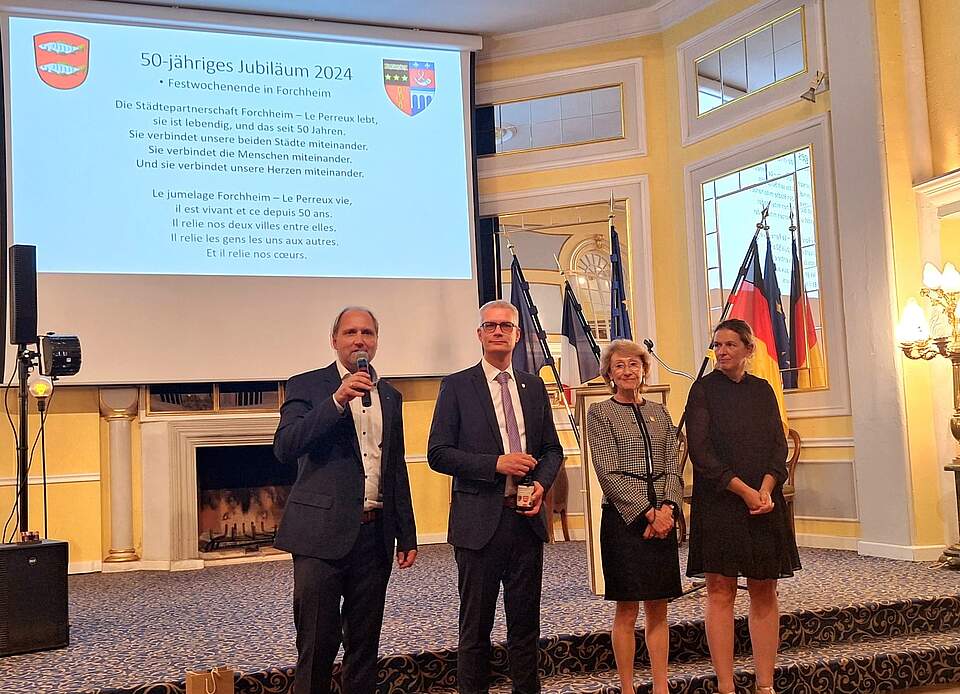 50 Jahre Städtepartnerschaft Le Perreux Dr. Uwe Kirschstein und drei weitere Personen stehen vor einer Leinwand