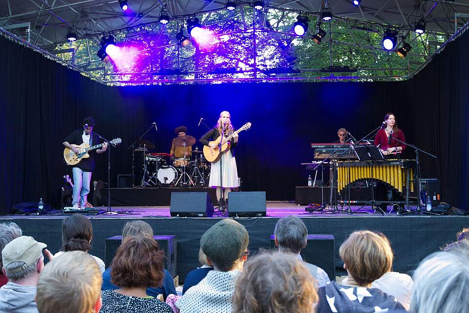 Band DOTA im KulturSommerQuartier Forchheim Eine Band spielt auf einer beleuchteten Bühne, im vor der Bühne sitzen Zuschauer.