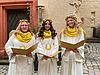 Drei junge Frauen in weißen Engelskostümen und goldenen Haarkränzen halten jeweils ein goldenes offenes Buch in ihren Händen.