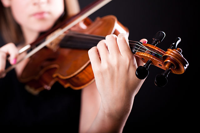 Eine Frau spielt Violine vor einem schwarzen Hintergrund.