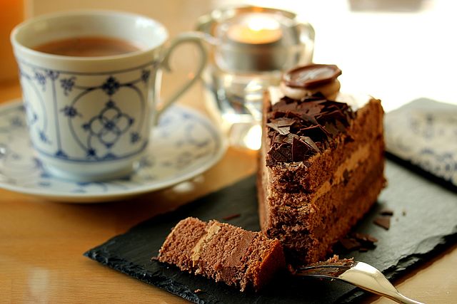 Eine Tasse Kaffee und ein Stück Schokoladentorte auf einer Schieferplatte stehen auf einem Tisch.