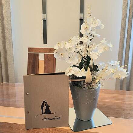 EIn helles Familiestandbuch steht mit einer weißen Orchidee auf einem Tisch.