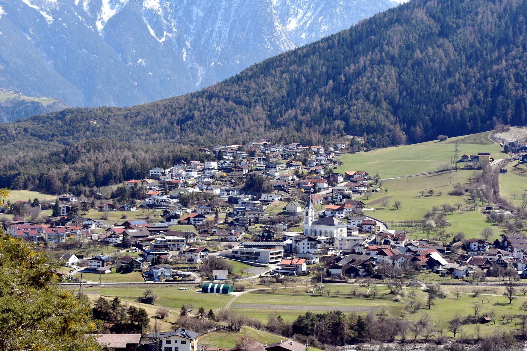 Ansicht von der österreichischen Partnerstadt Roppen mit schneebedeckten Berggipfeln im Hintergrund.
