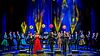 Musikerinnen und Musiker sowie Sängerinnen und Sänger in eleganter Abendgarderobe auf einer blau-gelb erleuchteten Bühne beim Auftritt.