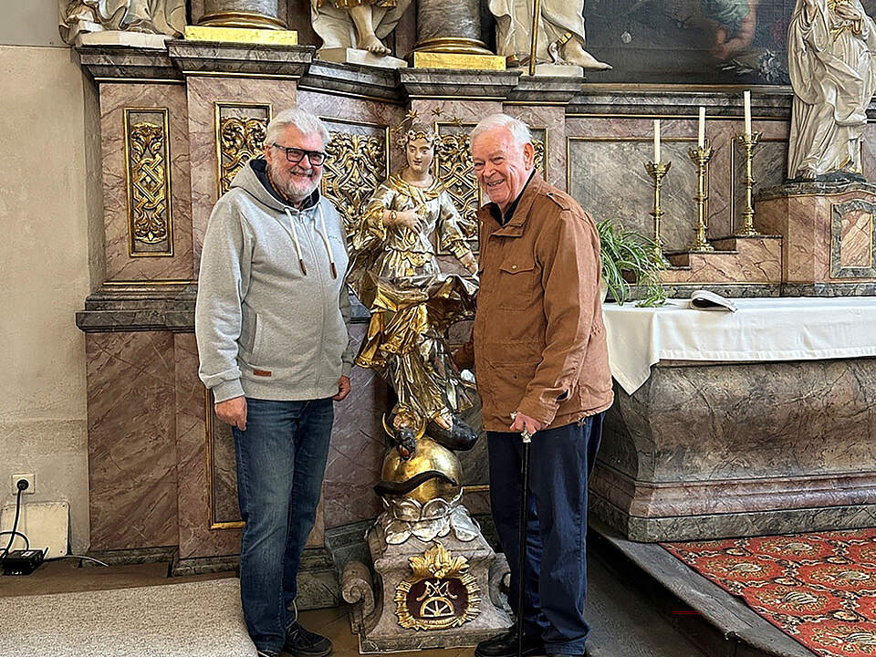 Zwei Personen in einer Kirche mit  einer Figur der Maria.