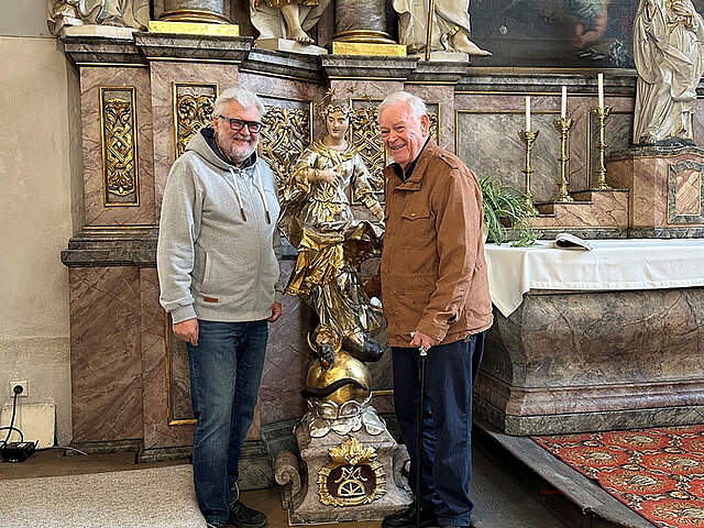 Zwei Personen in einer Kirche mit  einer Figur der Maria.