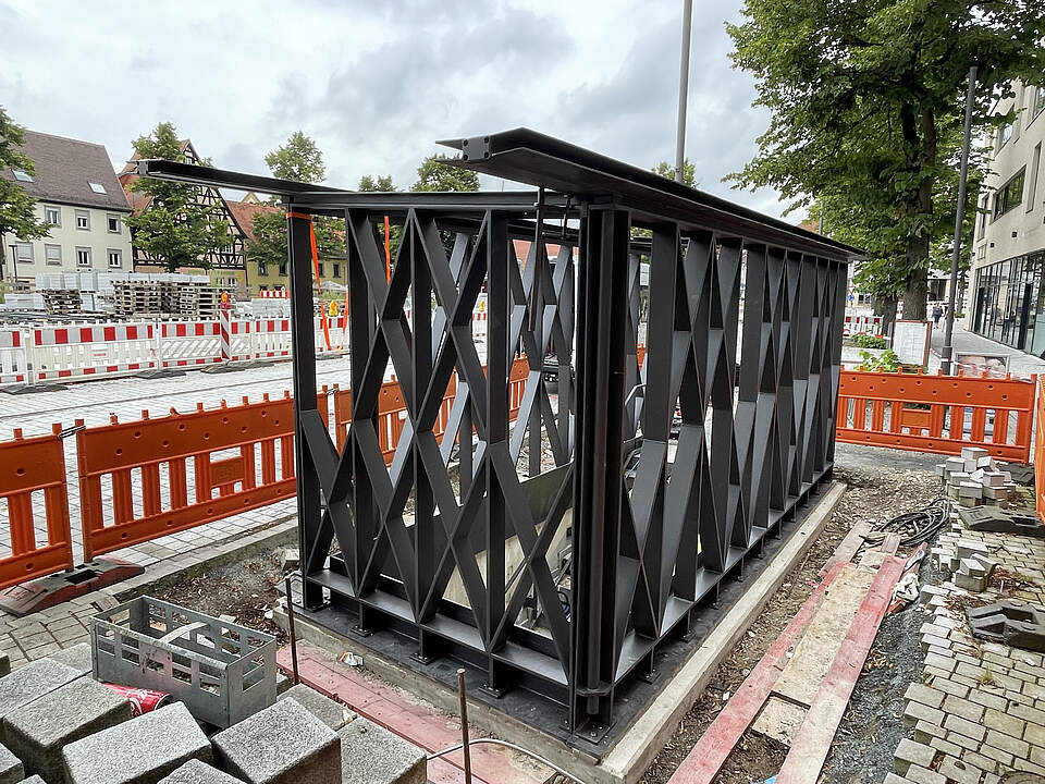 Hochbauten am Tiefagaragenabgang Süd am Paradeplatz Forchheim Ein moderner Hochbau aus dunklem Stahl wird gerade an einem Treppenabgang zu einer Tiefgarage errichtet. Umliegend befindet sich eine Großbaustelle mit Absperrungen und verschiedenem Baumaterial.
