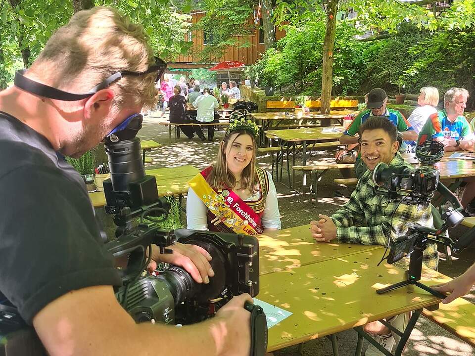 "Wunderschön" filmt im Forchheimer Kellerwald Ein Fernseh-Team dreht auf einem Bierkeller. Am Tisch sitzt die Forchheimer Bierkönigin Luisa I. in Tracht und mit Schärpe und Krone zusammen mit einem Morderator. Im Hintergrund befinden sich mehrere Biertischgarnituren mit weiteren Gästen.