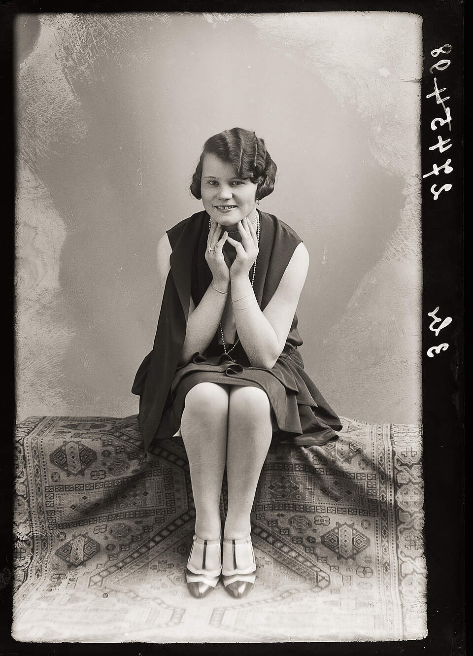 Eine schwarz-weiß Fotografie aus den 1920er Jahren zeigt eine Frau sitzend und mit auf Händen aufgestützten Kinn, die lächelnd in die Kamera blickt.