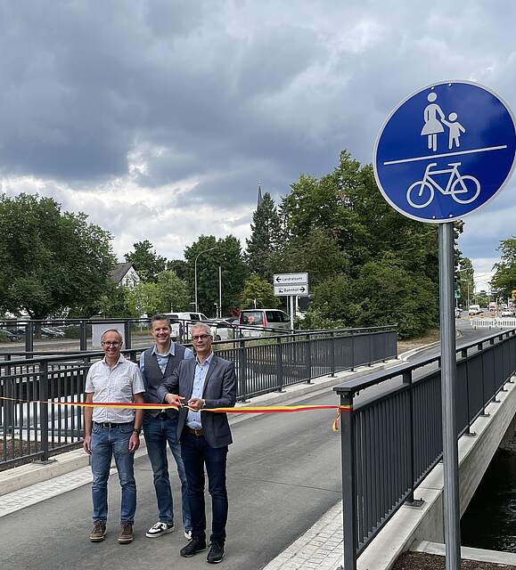 Personen auf einer Brücke, die ein Band zur Eröffnung durchschneiden.