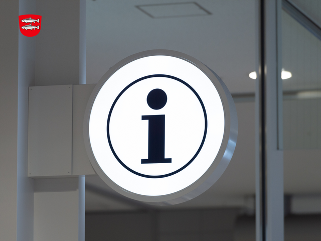 Ein Büro mit Glastrennung und einem beleuchteten runden Schild mit einem Info-Zeichen.