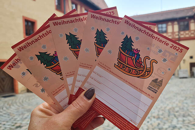 Eine Frau hält aufgefächerte Weihnachtslose in einer Hand. Im Hintergrund sieht man schemenhaft den Innenhof der Forchheimer Kaiserpfalz.