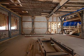 Innenansicht eines großen Raumes mit Stahlverband an der Außenwand, Aufhängungen und ein neuer Giebel auf einer Baustelle.