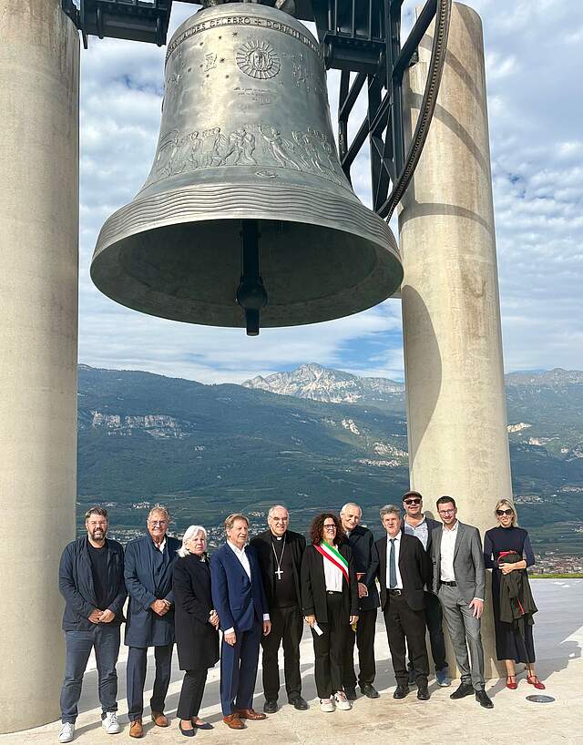 Die Forchheimer Delegation zusammen mit Vertretern der Stadt Rovereto und der Kirche unter der Friedensglocke. Im Hintergrund Berge und blauer Himmel mit Wolken.