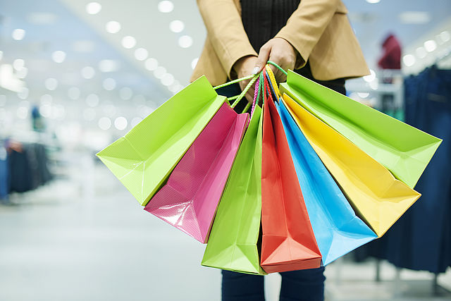 Eine Frau hält sieben farbige Einkaufstüten in einem Geschäft.