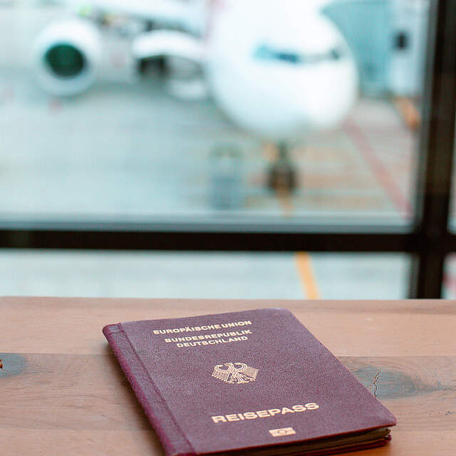 Reisepass auf einem Tisch an einem Flughafen mit Flugzeug im Hintergrund.