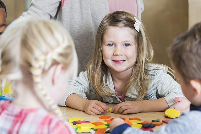 Kita Kinder am Tisch beim Spiel. Ein Mädchen blickt in die Kamera