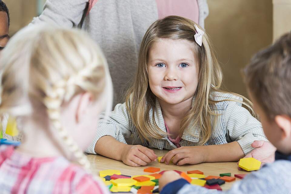Kita Kinder am Tisch beim Spiel. Ein Mädchen blickt in die Kamera