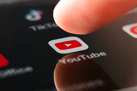 Ein Finger nähert sich zum Aktivieren der YouTube-App auf einem Handydisplay.