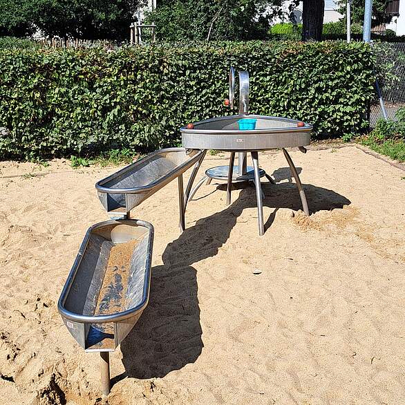 Ein mehrteiliges Wasserspielgerät in einem Sandkasten auf einem Spielplatz.