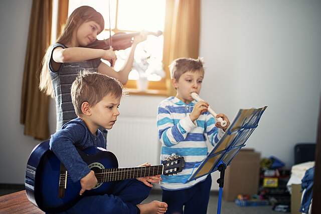 Drei Kinder musizieren in einem lichtdurchflutenden Raum