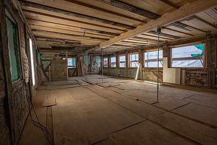 Das Foto zeigt eine Baustelle in einem großen Raum in einem historische Fachwerkgebäude. Die historische Holzdecke wurde saniert. Am Boden liegen provisorische Holzplatten.