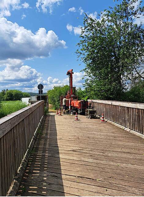 Arbeiten mit Bagger an einer sanierungsbedürftigen Holzfußgängerbrücke.