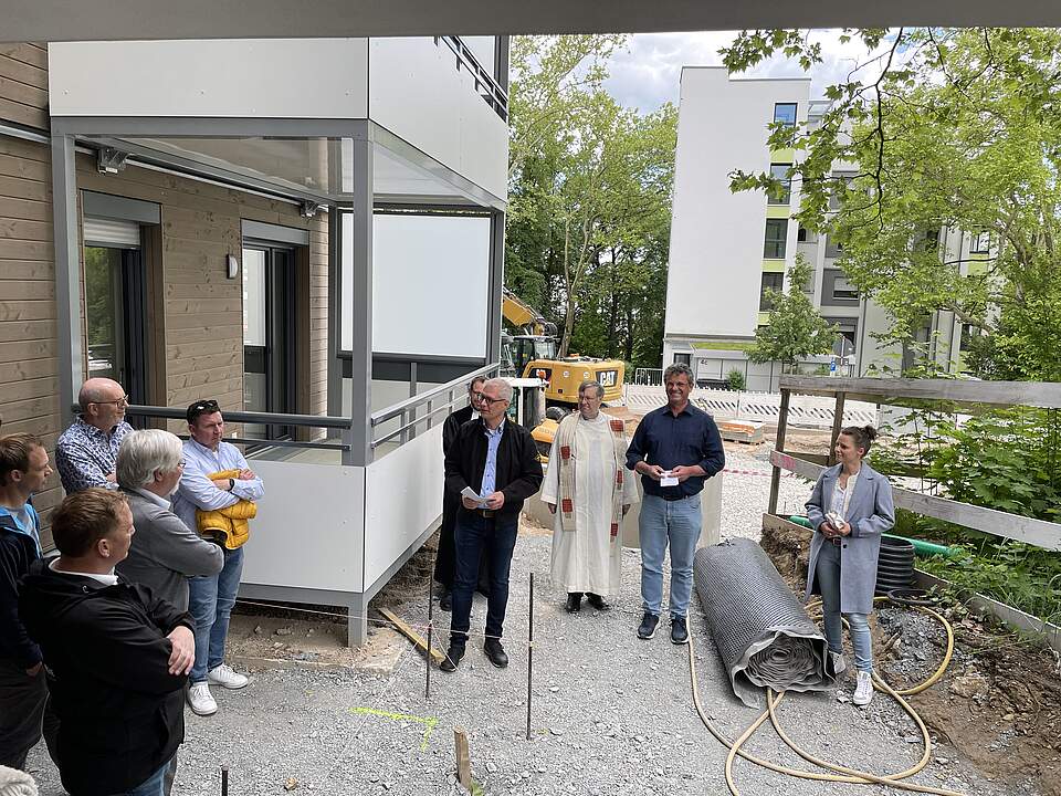 Mehrere Personen und Redner bei einer Einweihung eine modernen Wohnkomplexes vor dem neuen Gebäude.