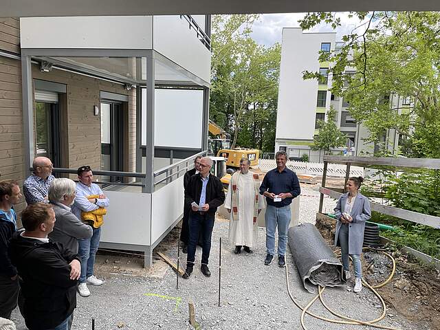 Mehrere Personen und Redner bei einer Einweihung eine modernen Wohnkomplexes vor dem neuen Gebäude.