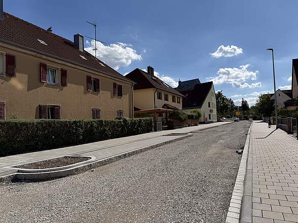 Neugestaltung Bammersdorfer Straße - Bauabschnitt 1_Parkbucht Ein Straßenzug mit Wohnhäuser, der umgestaltet wird. Pflaster und Untergrundarbeiten, sowie Parkbuchten sind fertiggestellt. Die Fahrbahn ist geschottert, die Teerdecke fehlt noch.