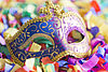 Eine venezianische Maske mit goldener Umrandung liegt auf buntem Papierschnipseln.